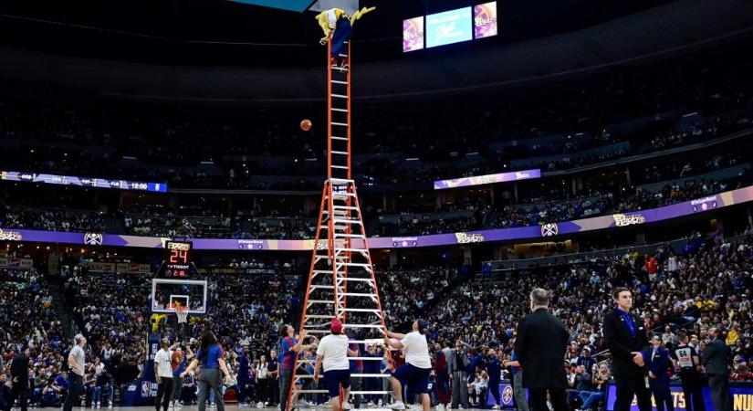 Létrán állva, a palánknak háttal dobott félpályás kosarat az NBA-csapat kabalafigurája