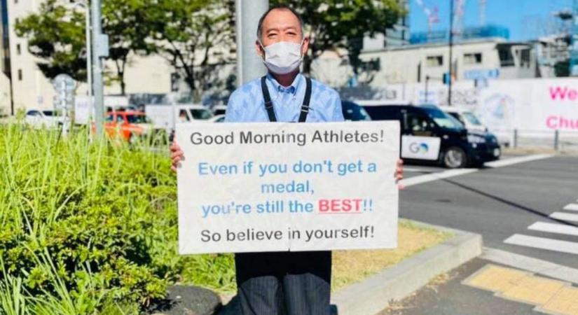 Ez a táblát tartó férfi a tokiói olimpia titkos csillaga
