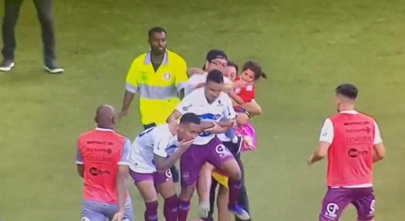 Kislányával a karján rohant a pályára egy férfi, hogy belerúghasson egy focistába - videó