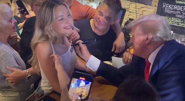 Trump választási pizzát osztott, majd aláírta egy nő felsőjét – videó