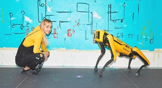 Festőnek állt egy robotkutya, egy másik fotózkodik a képekkel, a harmadik meg ezt a kettőt nézi