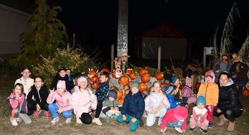 Narancssárga csodalámpások fénye világít a faragott kopjafánál Jásziványon